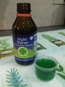 A bottle of NiteNurse with a cap full of the green medicine.