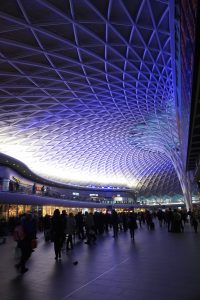 The blue designed ceiling at Kings Cross Station in London, England while passengers walk to their trains underneath it.