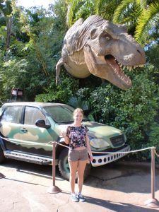 A girl smiles in front of a T-Rex model from Jurassic Park.
