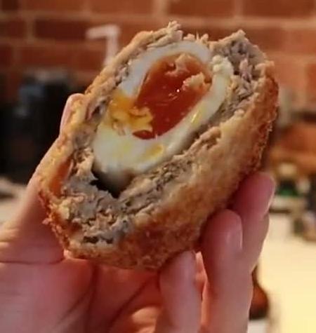 Cut Scotch egg showing its yolk and white, surrounded by meat and a crumb coating