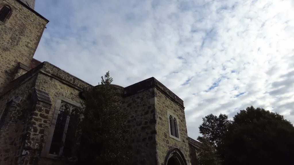 Stone walls and arched windows of St Nicholas Church in Pluckley beneath a cloudy sky