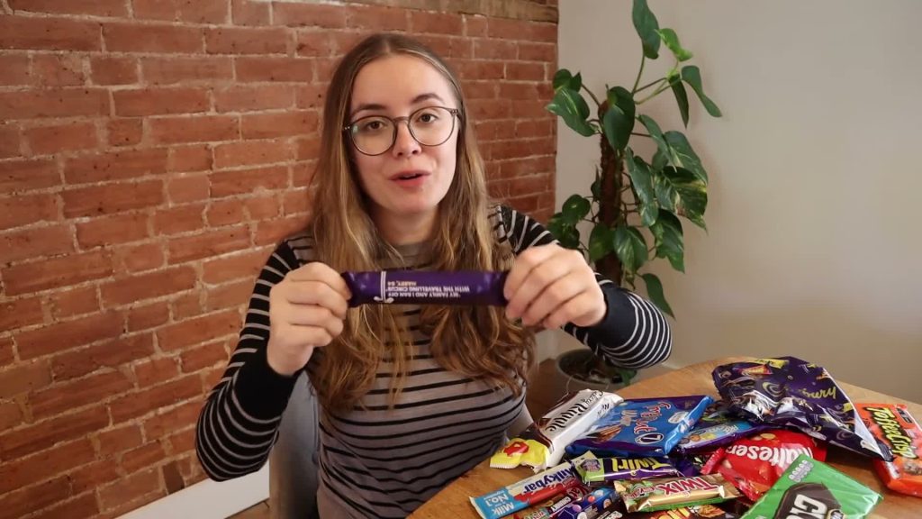 Alanna holding a purple chocolate wrapper above a table covered with chocolate bars and packets