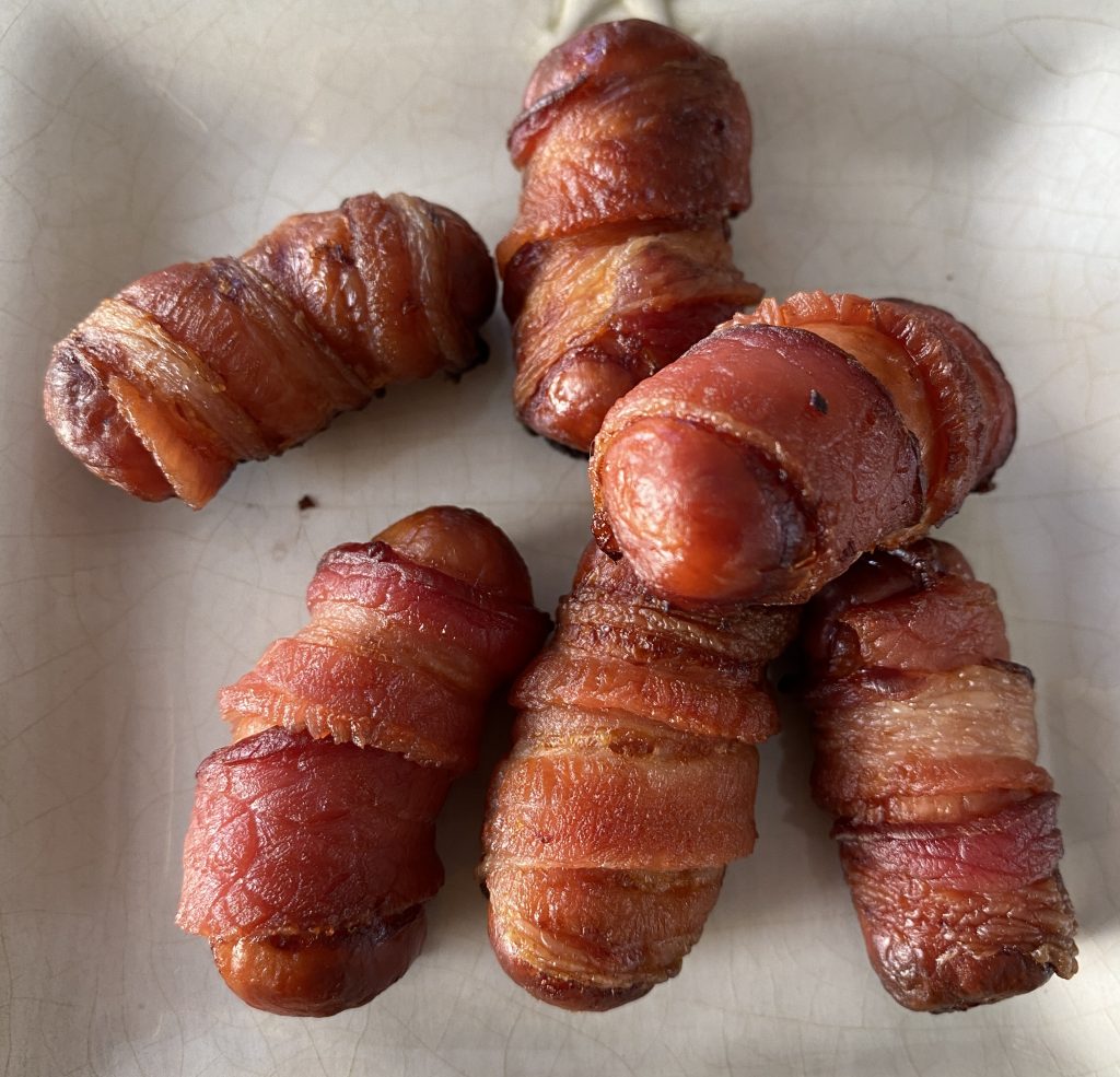 Cooked sausages wrapped in browned bacon on a plate