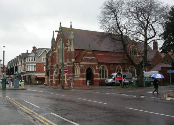 A Tesco Express sign above an arched entrance in a red-brick former church