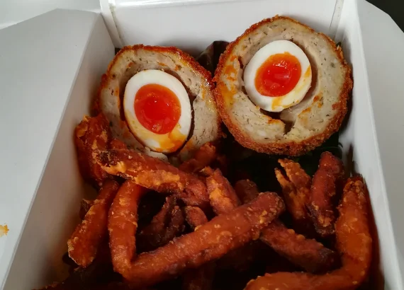 Two Scotch egg halves with orange yolks, shown above sweet potato fries in a food tray.