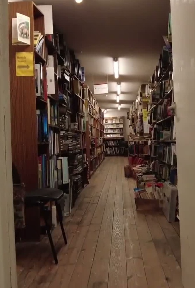 Narrow wooden-floor aisle between tall book-filled shelves at Baggins Book Bazaar