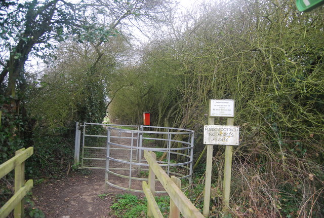 A metal kissing gate and a public footpath sign at the entrance to a wooded path in Hadlow