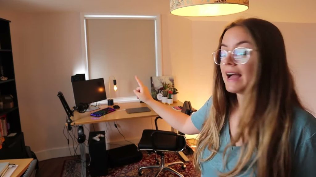 Alanna points towards a desk with a monitor, keyboard, microphone and computer tower in the home office