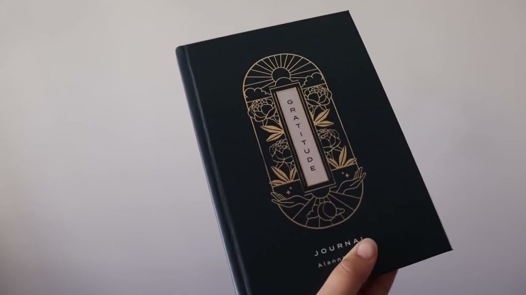 Alanna holding a dark gratitude journal with gold decoration on its cover