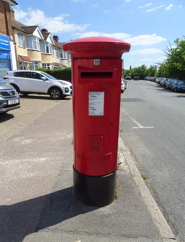 A red pillar postbox on a residential street, with Elizabeth II's royal cypher on its front.
