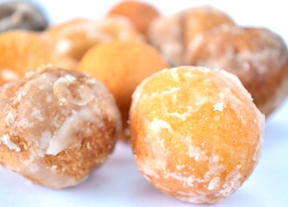 A close view of small round glazed Timbits doughnuts on a white surface