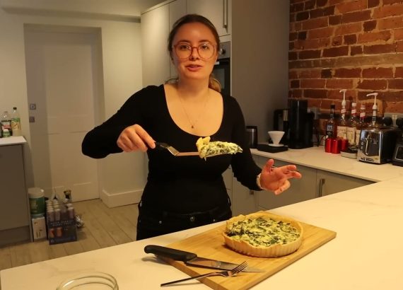 Alanna holds up a slice of her spinach quiche, with the remaining quiche on a chopping board