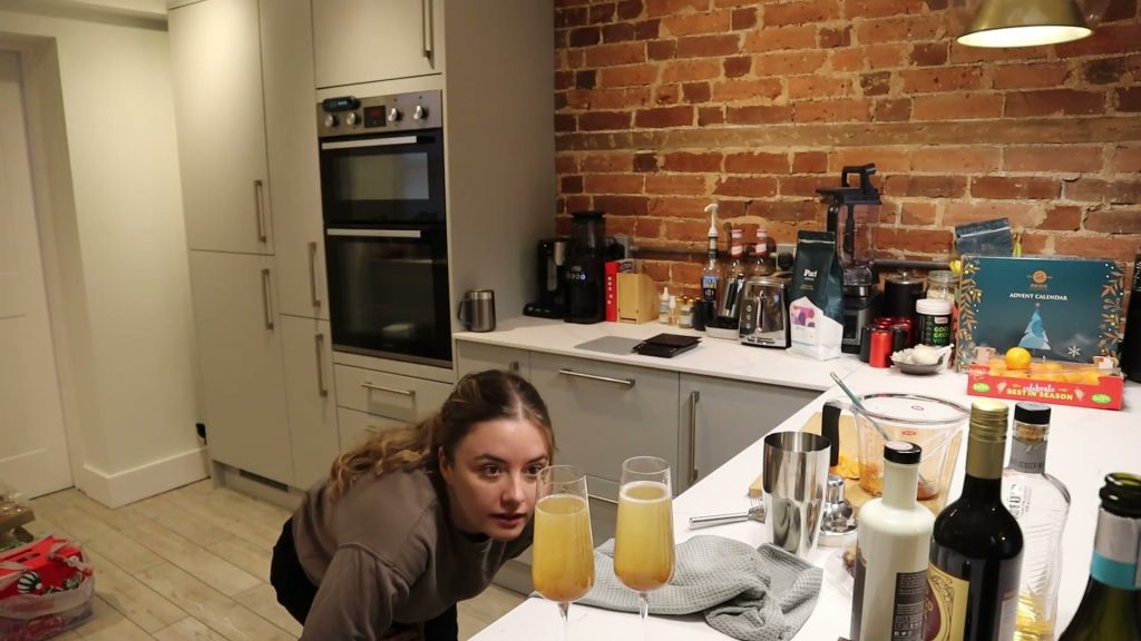 Two pale orange mimosas with brown syrup settled at the bottom, as Alanna looks at the glasses on her kitchen counter.