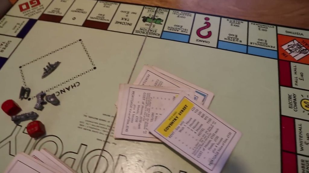 An angled view of my vintage British Monopoly board with property cards, playing pieces and red dice