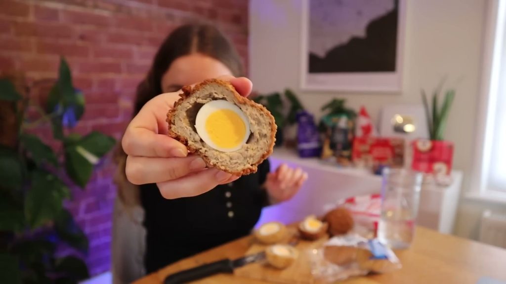 Alanna holding a cut Waitrose Scotch egg close to the camera, with the egg and meat filling visible