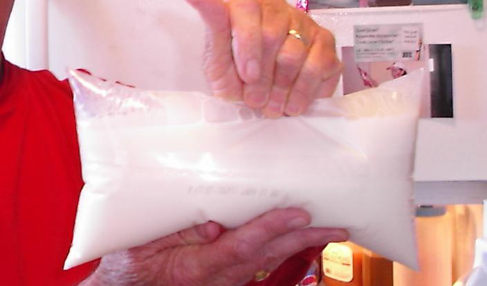 A hand holding a sealed white plastic bag of milk.