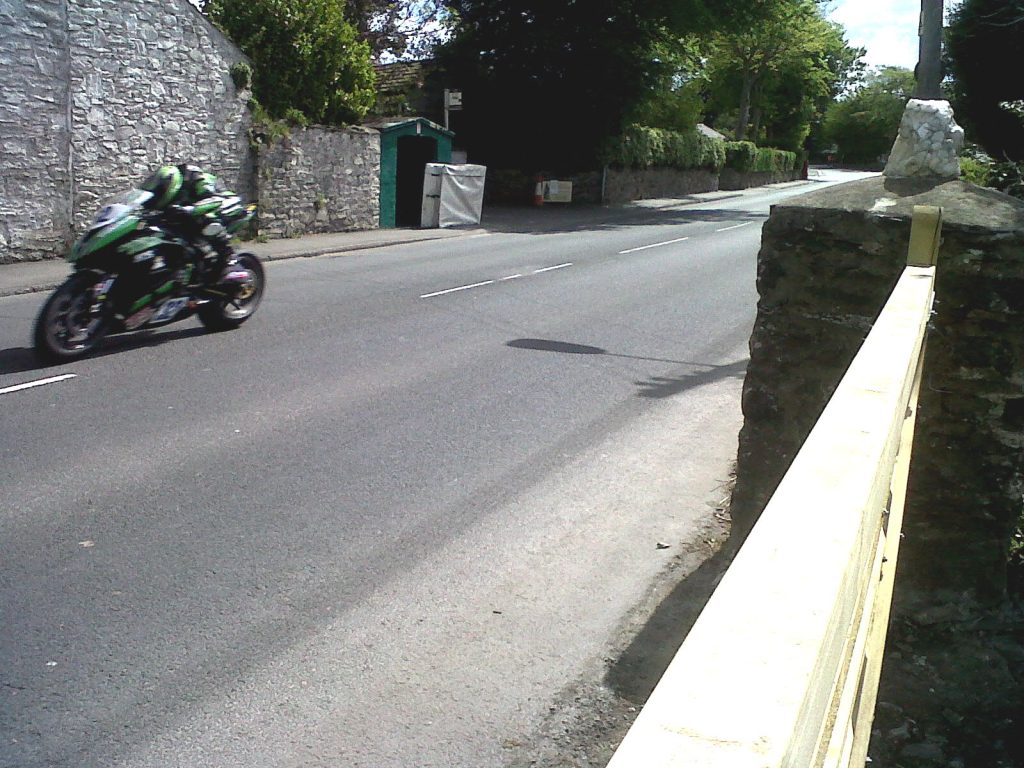 A motorcycle rider passing stone buildings and walls on an ordinary road at Ballagarey.