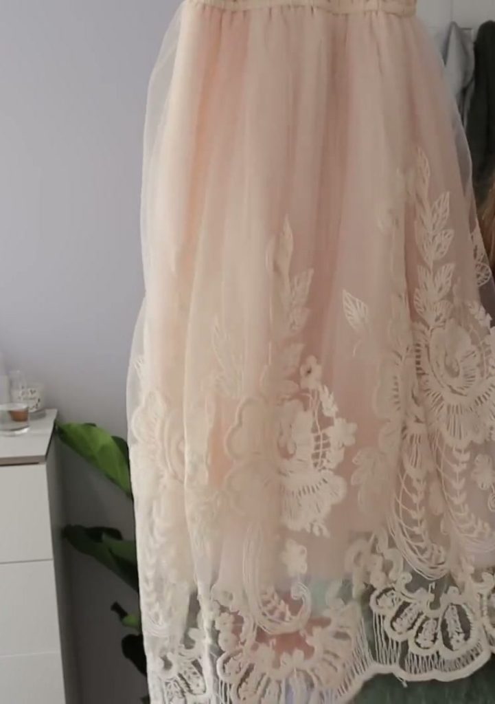 Peach-coloured dress fabric with floral embroidery and a scalloped hem.
