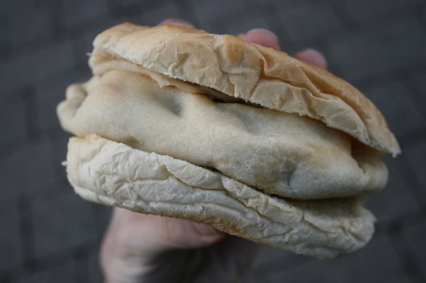 A pasty inside a soft bread roll, held in a hand