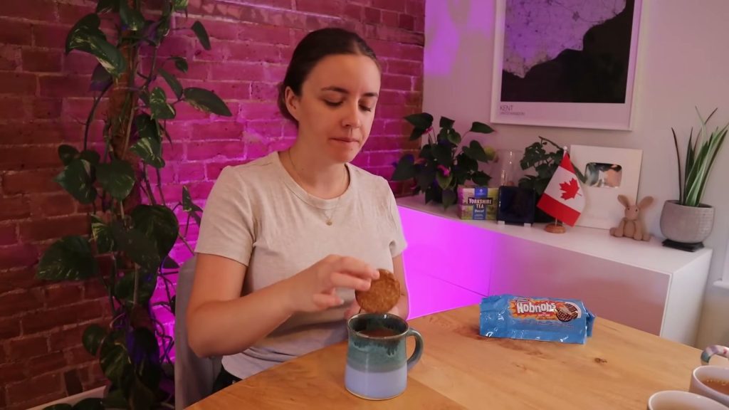 Alanna lowers a milk chocolate Hobnob towards a mug of tea, with its packet on the table.