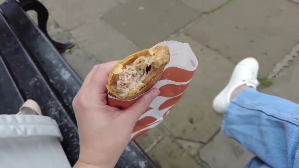 A bitten sausage roll shows its meat filling inside a paper bag.