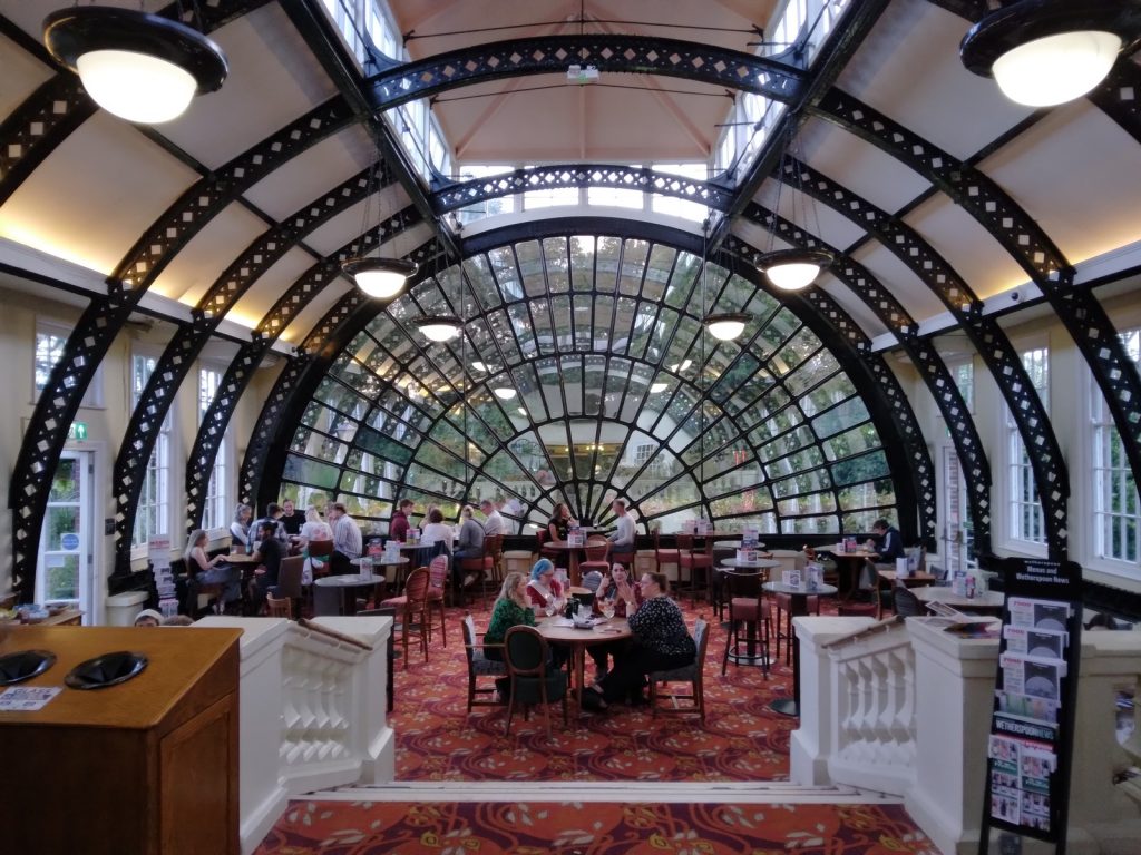 Iron arches and a large semicircular window over tables inside the Imperial pub's orangery in Exeter.