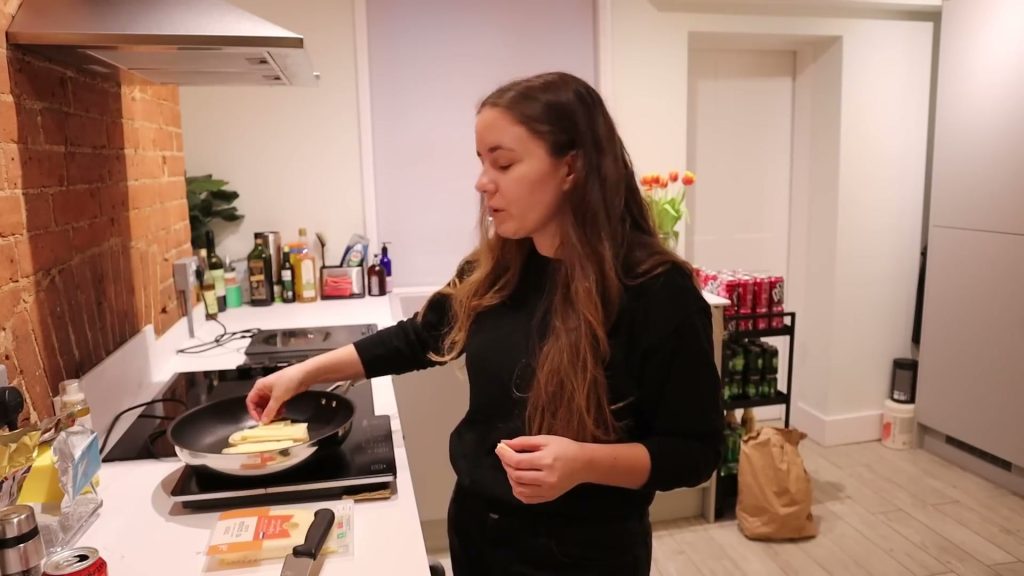 Alanna arranges cheese on bread in a frying pan on the hob.