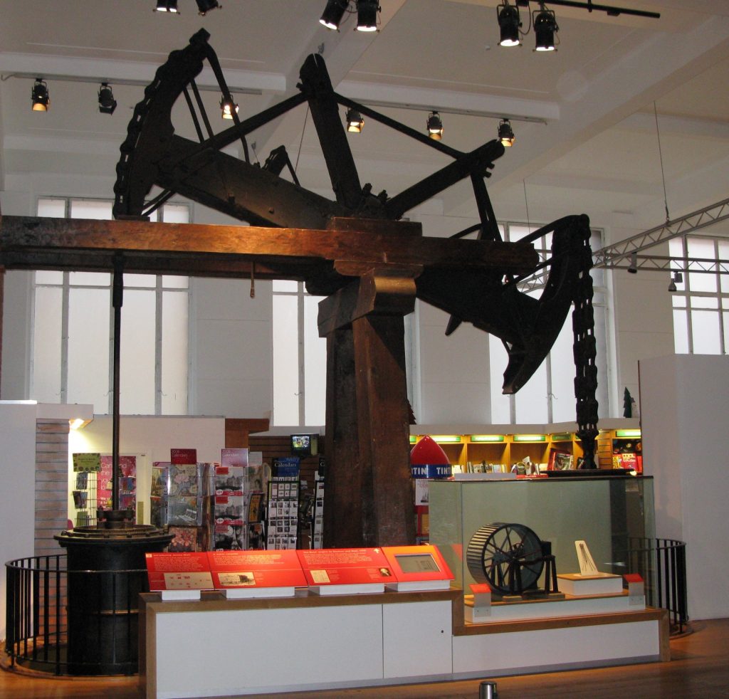 Old Bess beam engine displayed indoors, with a large wooden beam, chains and a cylinder.