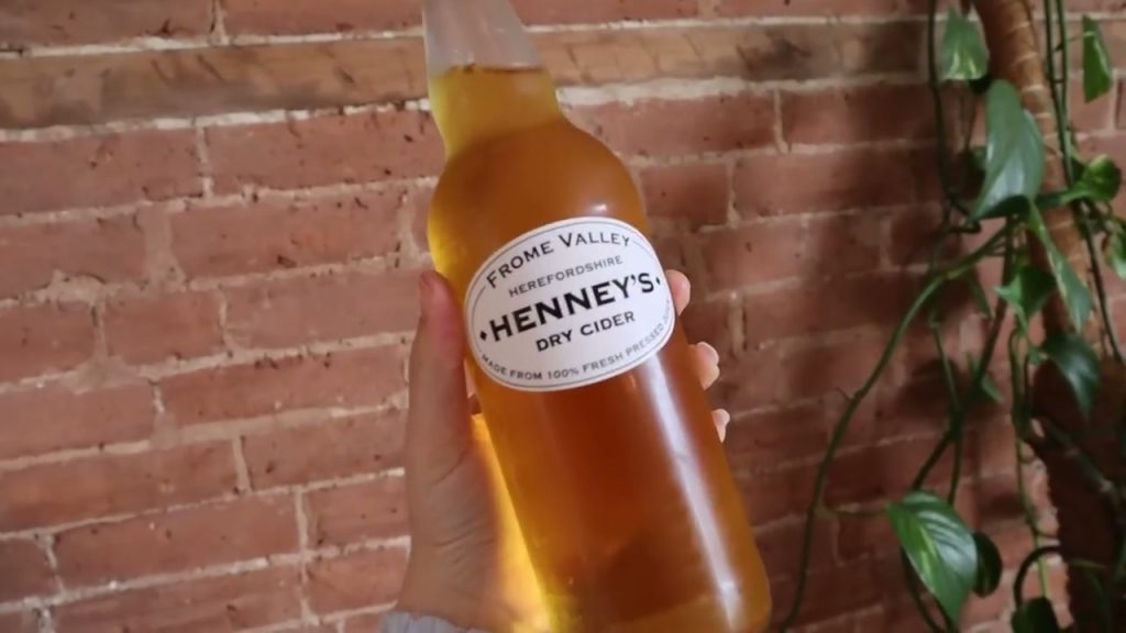 A bottle of Henney's dry cider held in front of a brick wall.