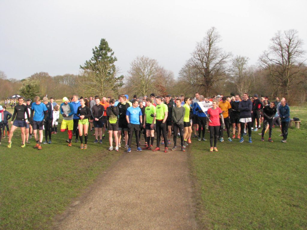 Runners gather on grass at the start of Nonsuch parkrun beside a path and winter trees.