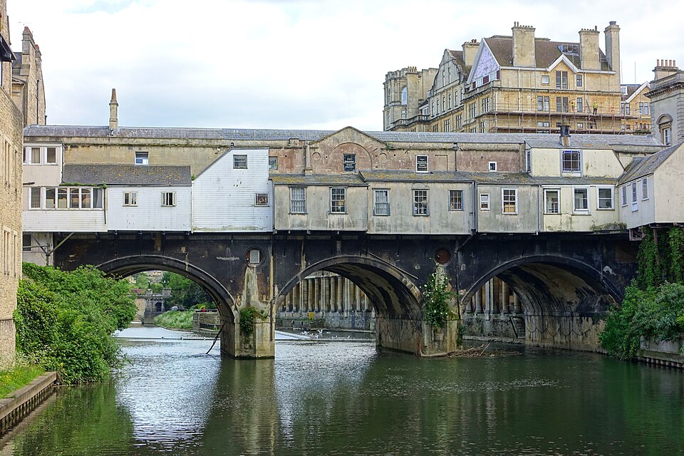 Rear view of Pulteney Bridge in Bath, with buildings above three stone arches over the River Avon.