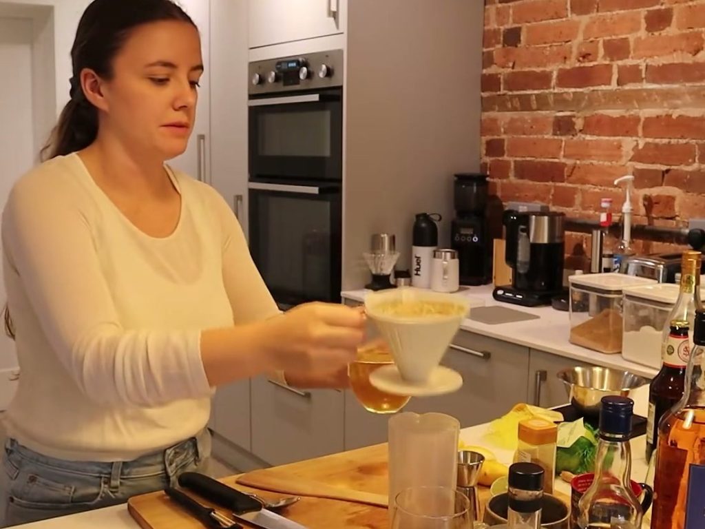 Alanna holds a coffee dripper containing curds beside a glass of clarified milk punch.