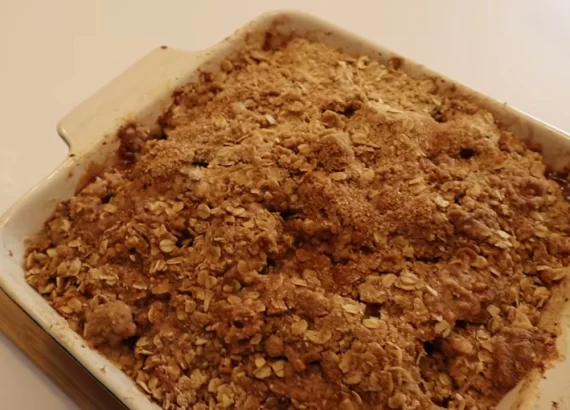 A baked apple crumble with a brown crumb topping in a rectangular cream dish.
