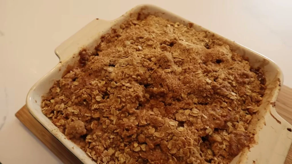 A baked apple crumble with a brown crumb topping in a rectangular cream dish.